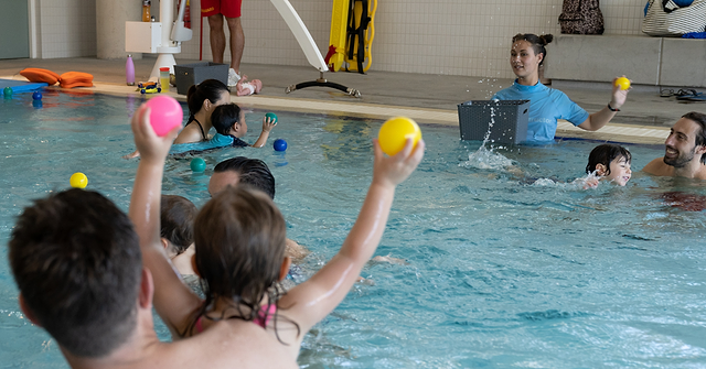 Swimming instructor running a swimming lesson with a group of children and their parents