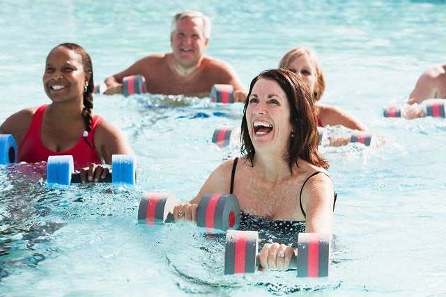 A group of people smiling while using floating dumbbells in an aqua aerobics class