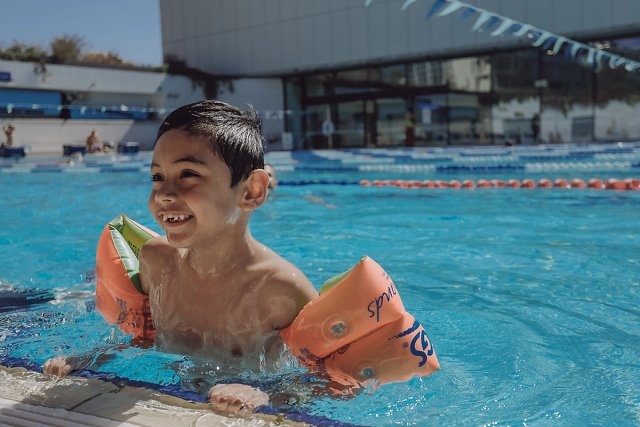 Boy in the pool at Gunyama Park smiling and wearing floaties 