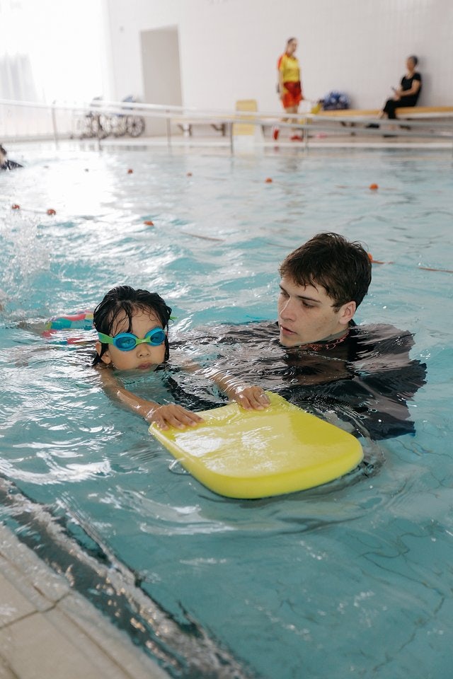 Swimming instructor running a swimming lesson with a child holding a kickboard