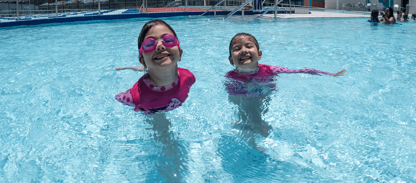 Two kids smile while swimming outdoors in the 50m pool at Gunyama Park