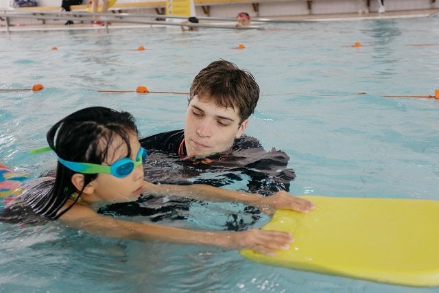 Swimming instructor running a swimming lesson with a child holding a kickboard